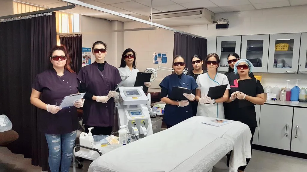 A group of aesthetic students in Birmingham receiving hands-on laser treatment training in a professional clinical setting.